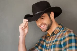 39146815 smiling cowboy handsome young man adjusting his cowboy hat and smiling while standing against grey b 300x200